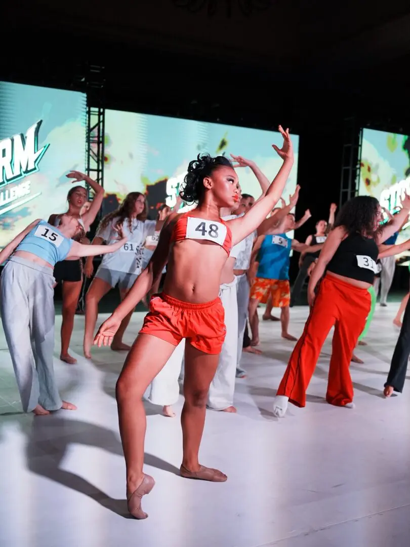 A woman in orange shorts and a sports bra dances energetically on stage.