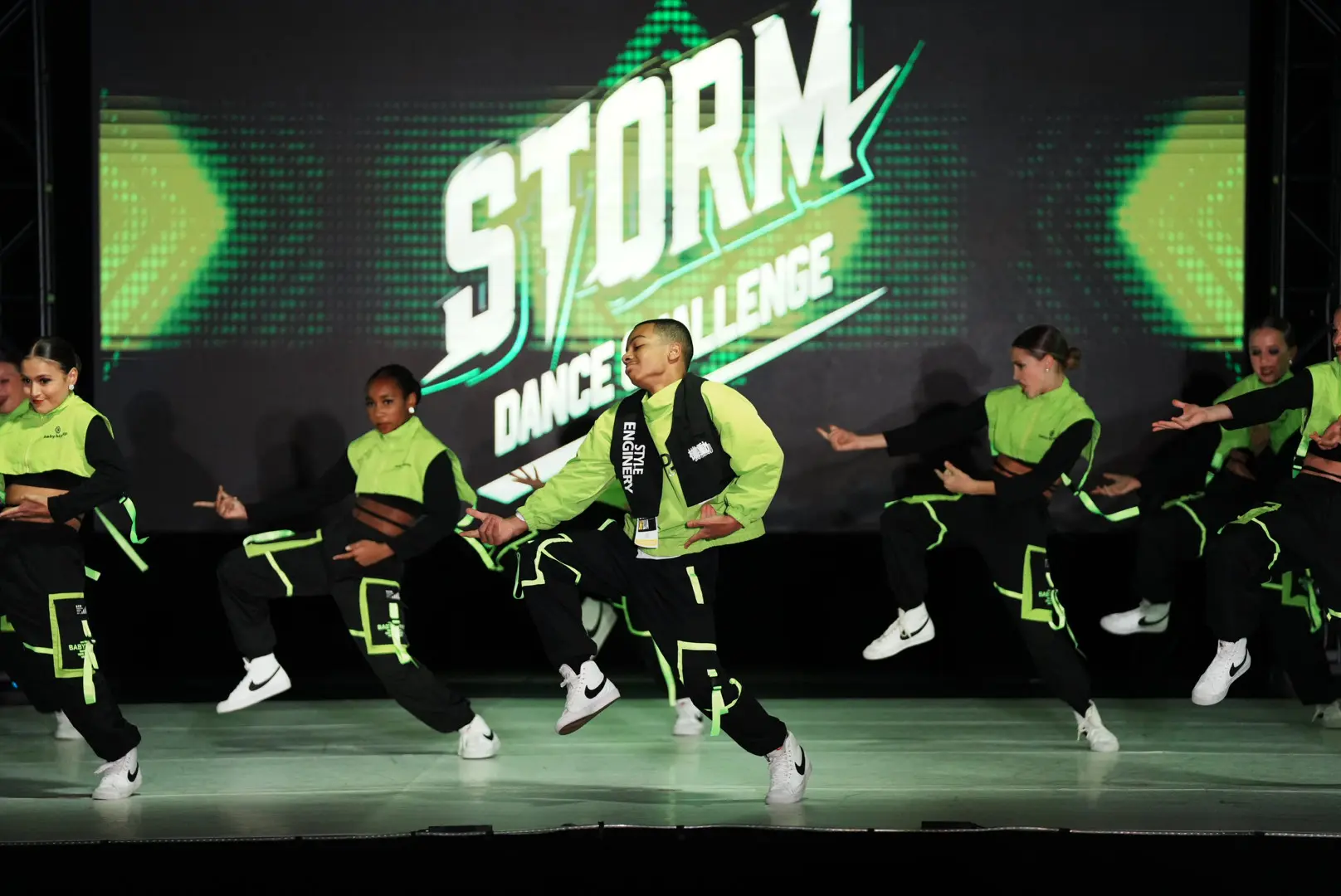Dynamic dance crew performing energetically on stage in neon green and black outfits.